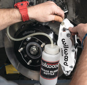 Wilwood installation example showing a bleed bottle connected to a white brake caliper beside a rotor