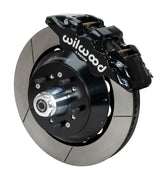 Wilwood AERO6 brake kit: A black caliper beside a slotted rotor and deep black hat over a wheel hub, with visible studs and a polished dust cap; 14-inch front brake setup for 1957–1967 F-100.