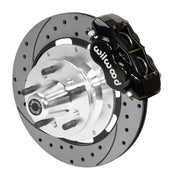 Wilwood black four-piston front caliper beside a 12.19-inch drilled-and-slotted rotor with projecting wheel hub for the early A-body 12.19-inch front installation