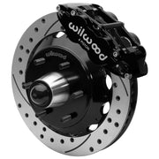 Wilwood black front caliper beside the assembled 13.06-inch drilled and slotted rotor for the Chevrolet/GMC six-lug 13.06-inch Superlite drop-spindle brake conversion, with the hub and wheel studs visible