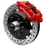 Wilwood red front caliper beside the assembled 13.06-inch drilled and slotted rotor for the Chevrolet/GMC six-lug 13.06-inch Superlite drop-spindle brake conversion, with the hub and wheel studs visible